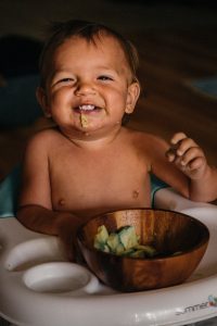 Topless baby smiling while eating