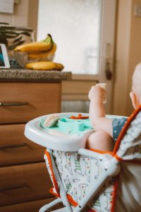 Baby in hi-chair with food in hand
